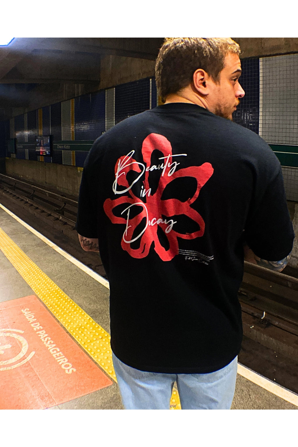 Modelo de costas vestindo camiseta Flower mostrando a estampa floral vermelha em contraste com o fundo preto